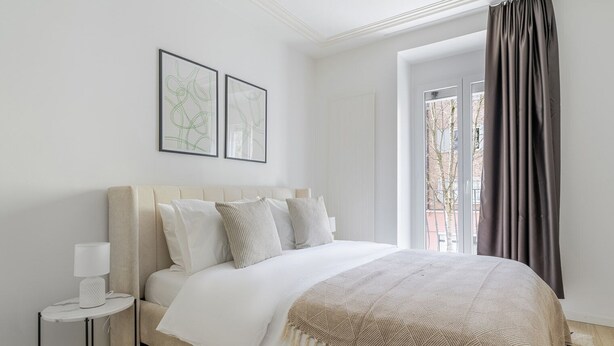 A bedroom with a bed, a bedside table, a lamp, and a window with curtains.