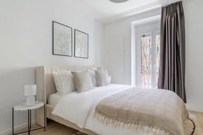 Een slaapkamer met een bed, nachtkastje, lamp en raam met gordijnen.