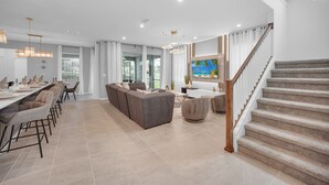 A spacious living area with a dining setup, a sofa, and a staircase. - Stunning 6 Bed Pool Home with Game Room-2386SWW (Kissimmee)