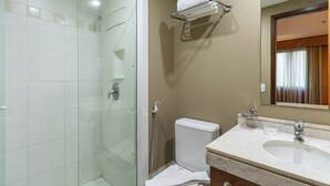 Un baño con ducha envuelta en vidrio, inodoro blanco y lavamanos de mármol.