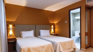 Habitación de hotel con dos camas, pisos de madera y un baño a la vista a través de una puerta abierta.