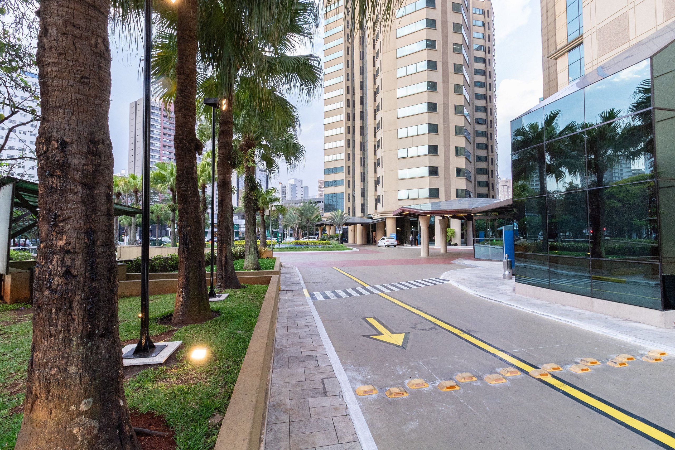 Uma rua urbana moderna com calçada para pedestres, edifícios altos e palmeiras.