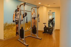 Ginásio com equipamentos de exercício, esteira e parede com um mural de uma pessoa a andar de bicicleta.