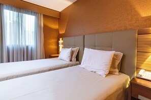 Een hotelkamer met twee bedden, een nachtkastje met een lamp en een raam met gordijnen.