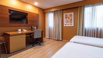 Quarto de hotel com escrivaninha de madeira, televisão de tela plana, cama e janela com cortinas.