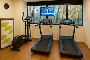 Une salle de remise en forme équipée de tapis de course, d’un vélo elliptique et d’un écran de télévision diffusant un programme d’information.