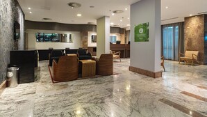 Un vestíbulo moderno con suelo de mármol, zona de estar con sillas de madera, mostrador de recepción y un gran ventanal.