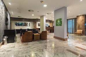 A modern lobby with a marble floor, seating area with wooden chairs, a reception desk, and a large window.