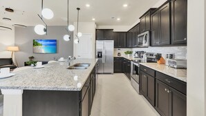 A modern kitchen with dark cabinets, a granite countertop, stainless steel appliances, and pendant lighting.