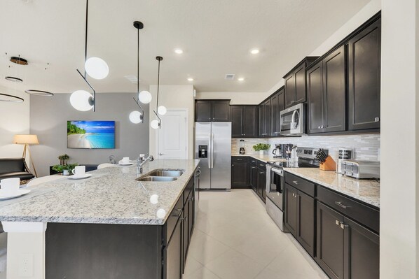 A modern kitchen with dark cabinets, a granite countertop, stainless steel appliances, and pendant lighting.