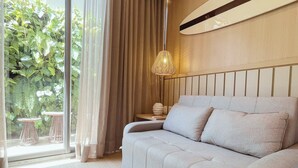 A modern bedroom with a sofa, a hanging light fixture, and a view of greenery outside. - Setai Yacht - Garden III - By Almare (João Pessoa)