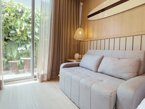 A modern bedroom with a sofa, a hanging light fixture, and a view of greenery outside. - Setai Yacht - Garden III - By Almare (João Pessoa)