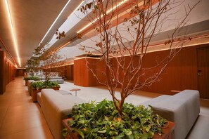 Un hall d’entrée moderne avec un long comptoir d’accueil, des espaces de détente et des plantes en pot.