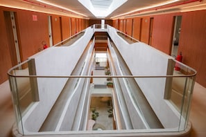 A modern hotel corridor with glass railings, a central staircase, and orange textured walls. - Setai Yacht - Garden III - By Almare (João Pessoa)