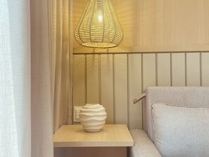 Un rincón de una habitación con un panel de pared de madera, un jarrón blanco sobre una mesita de madera y un sofá de color claro.