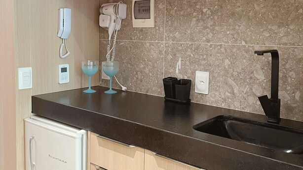 A kitchen with a black countertop, a sink, a hairdryer, and two blue glasses. - Setai Yacht - Garden III - By Almare (João Pessoa)
