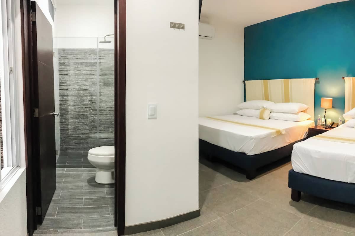 A hotel room with two beds, a bathroom with a shower, and a toilet.