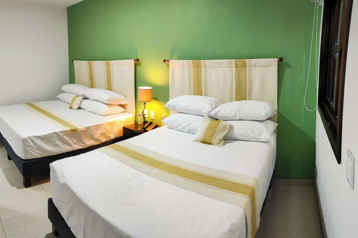 A hotel room with two single beds, a nightstand with a lamp, and a green wall.