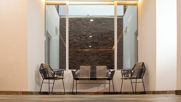Un interior moderno con un separador de vidrio, dos sillas tejidas negras y una pared con textura de piedra.
