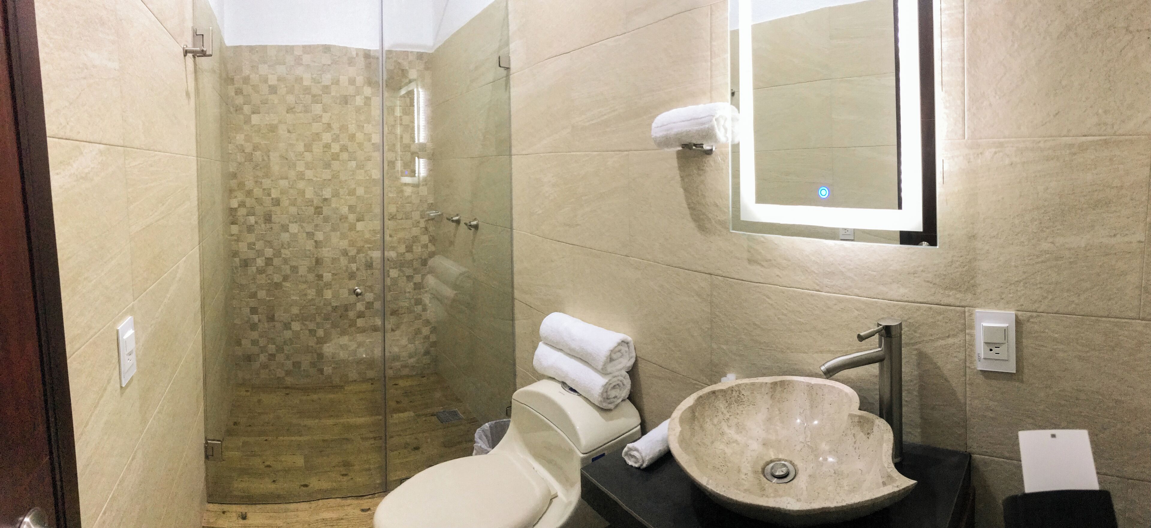 Un baño con ducha envuelta en vidrio, un lavabo, un inodoro y un perchero con toallas.