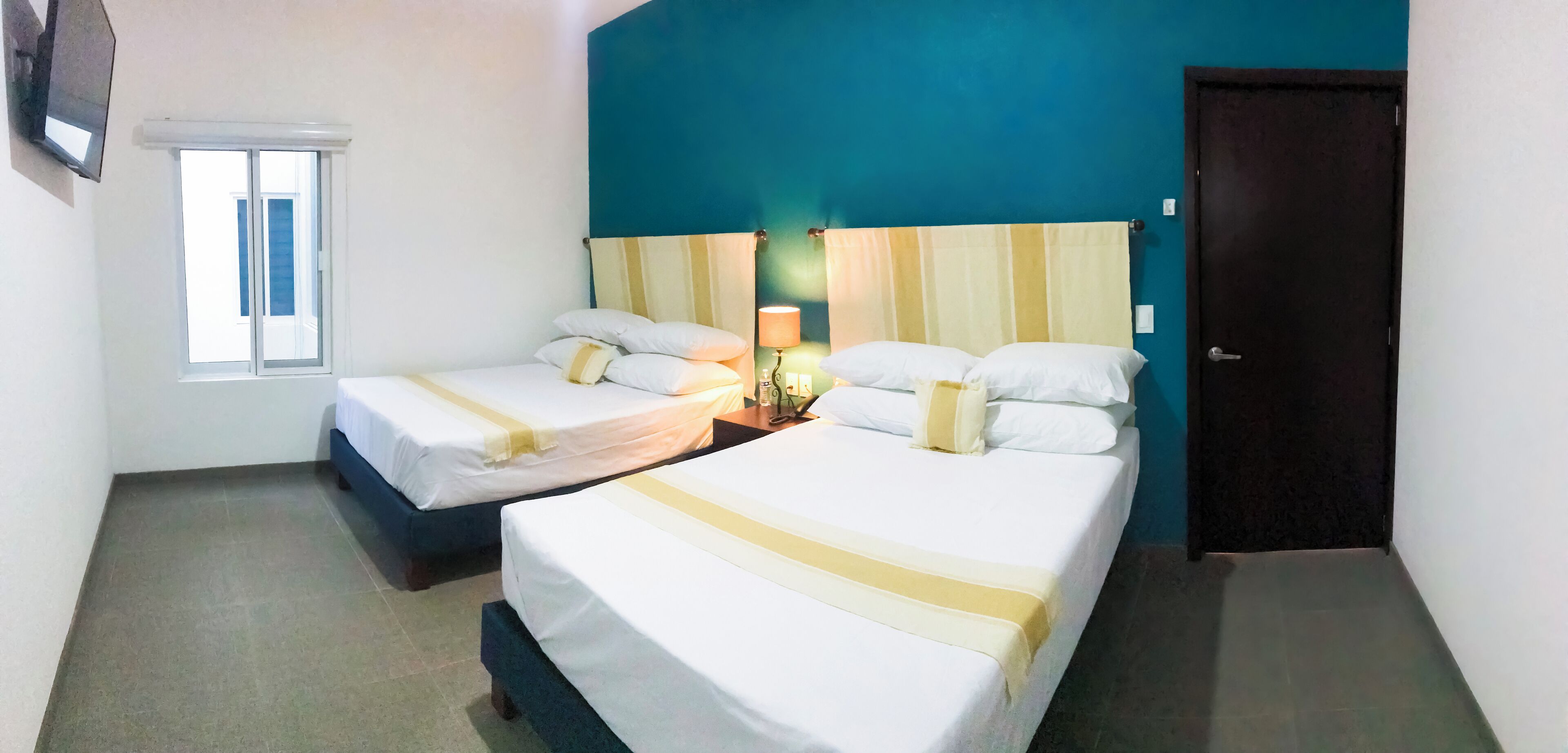 Una habitación de hotel con dos camas, una ventana, una puerta y un televisor montado en la pared.