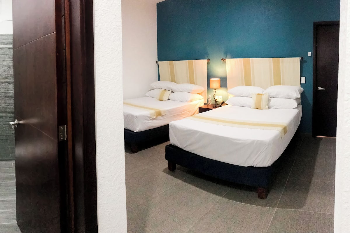 A hotel room with a shower, two beds, a nightstand, and a bathroom with a toilet.