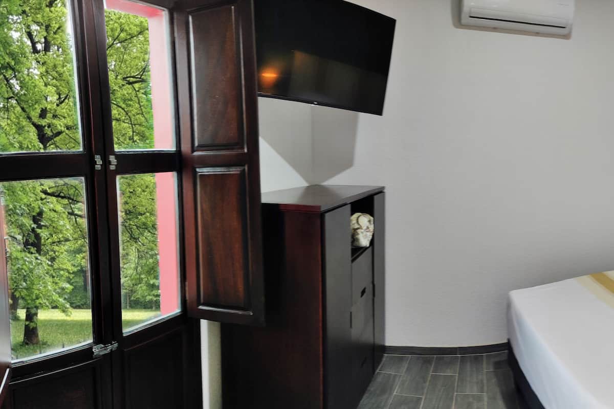 A hotel room with a bed, a TV mounted on the wall, a bedside table with a lamp, and a door.