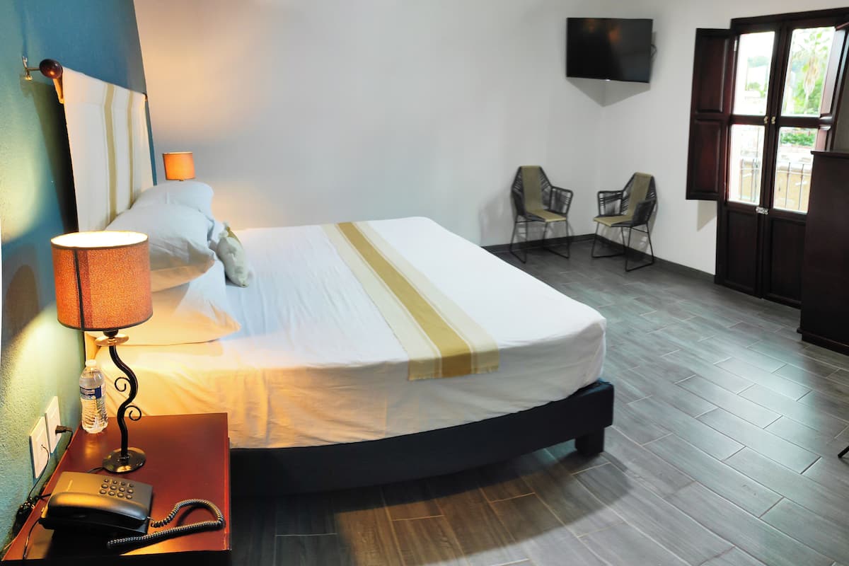 A hotel room with a bed, bedside lamp, telephone, and a desk with a bottle of water.