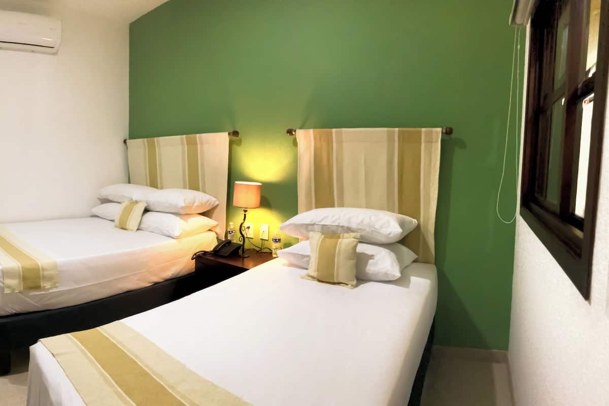 A hotel room with two beds, a bedside table with a lamp, and a window with curtains.
