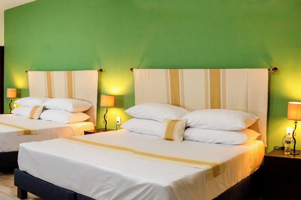 A hotel room with two beds, green walls, and bedside lamps.