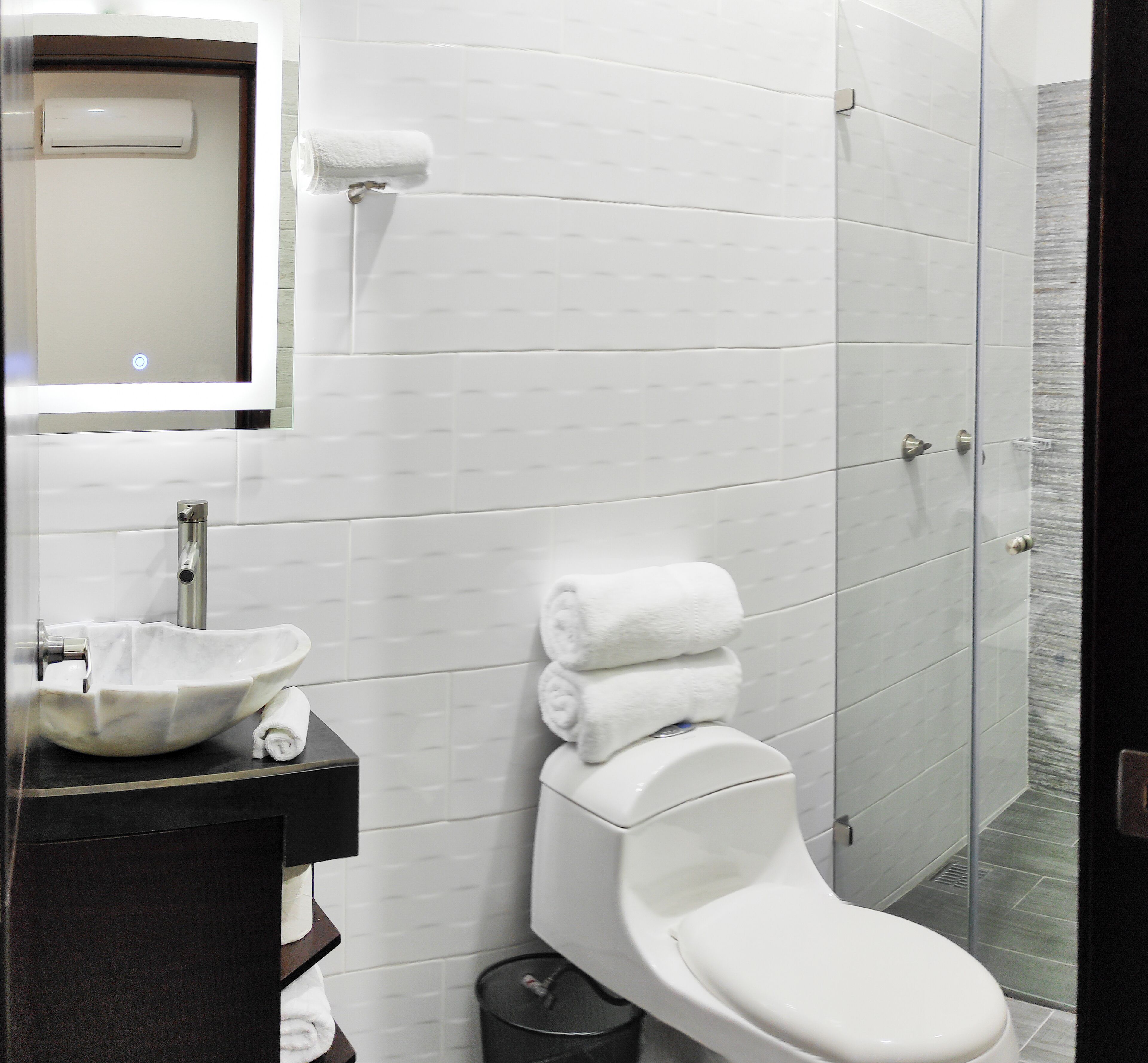 A modern bathroom with a white toilet, a sink with a marble basin, and a glass shower enclosure.