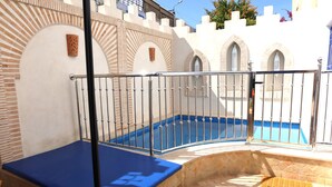 Zona de piscina con piscina azul, baranda metálica y pared de piedra con arcos.