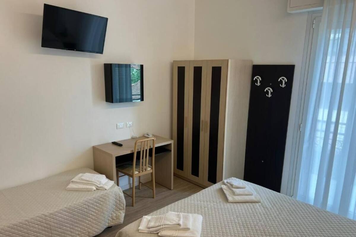 Camera d'albergo con due letti, una scrivania, una sedia, una TV e un armadio.