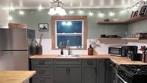 Une cuisine moderne équipée d’un réfrigérateur à deux compartiments, d’un évier double, d’une cuisinière et d’un four à micro-ondes. On y trouve également des tabourets de bar et une table en bois.