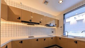 A modern kitchen with beige cabinets, white subway tiles, and a large window providing a view of the outside. - CJIA Apartment Hotel (Shanghai Zhongtan Road Subway Station) (Shanghai)