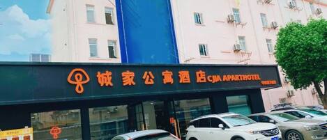 A hotel entrance with a signboard, multiple parked cars, and a building facade.