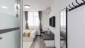 A compact hotel room with a bed, a small desk, a chair, a TV, and a coat rack. - CJIA Apartment Hotel (Shanghai Zhongtan Road Subway Station) (Shanghai)