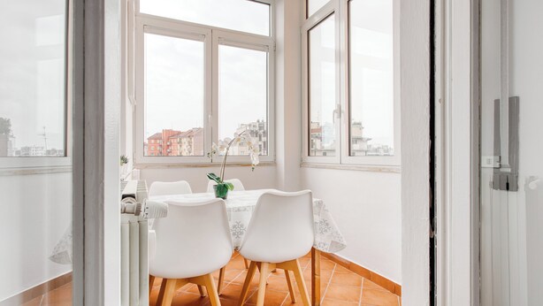 A dining area with a table and chairs, a potted plant, and a view of buildings through large windows. - Deltico; 4 guests in washington area (Milano)