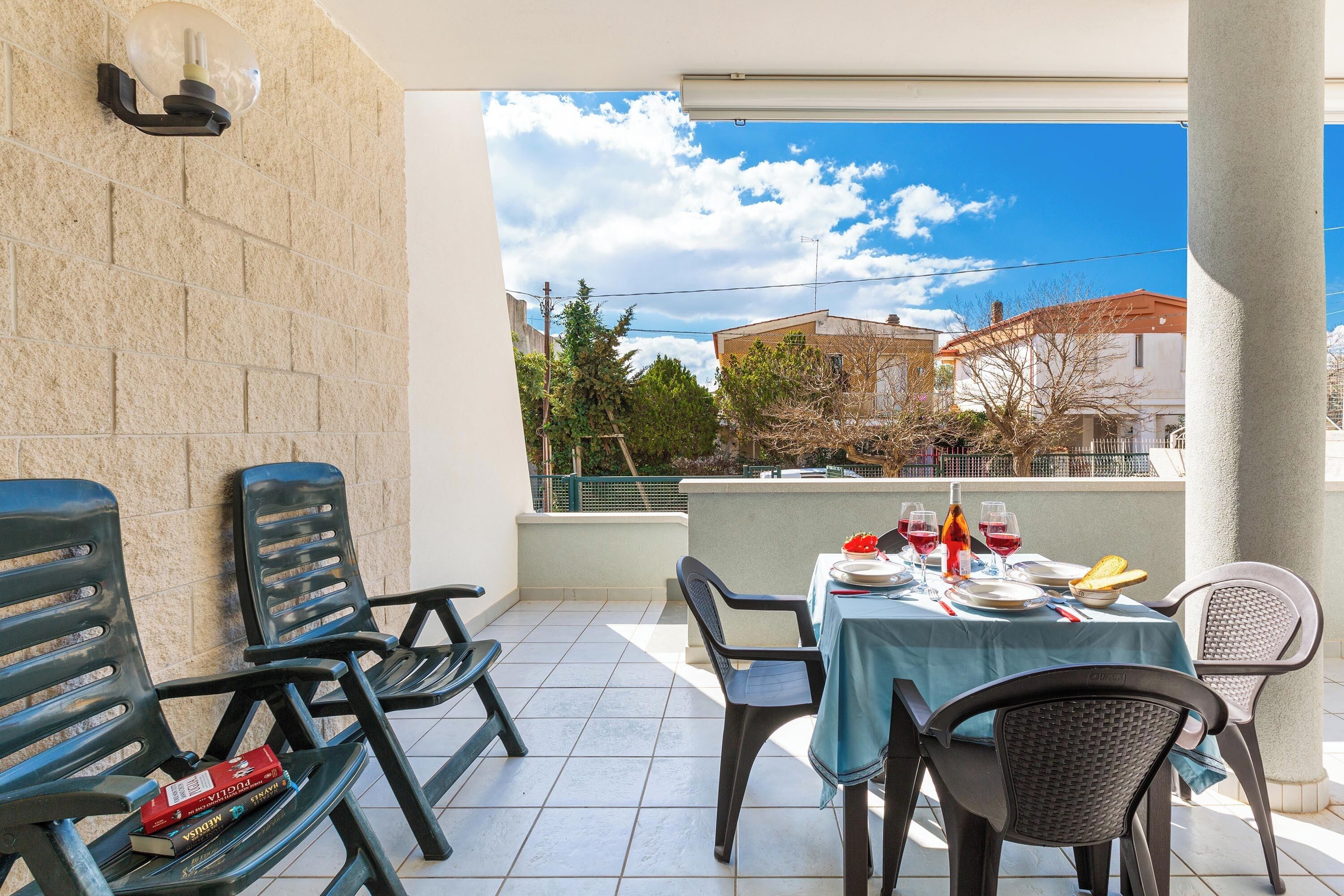 A balcony with a table set for dining, chairs, and a view of buildings and trees.