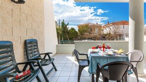 A balcony with a table set for dining, chairs, and a view of buildings and trees. - Residence Le Terrazze - Villino (Porto Cesareo)