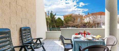 A balcony with a table set for dining, chairs, and a view of buildings and trees.