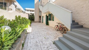 A narrow, paved courtyard with a stone wall on one side and a building with a staircase on the other. A bicycle is parked near the building. - Residence Le Terrazze - Villino (Porto Cesareo)