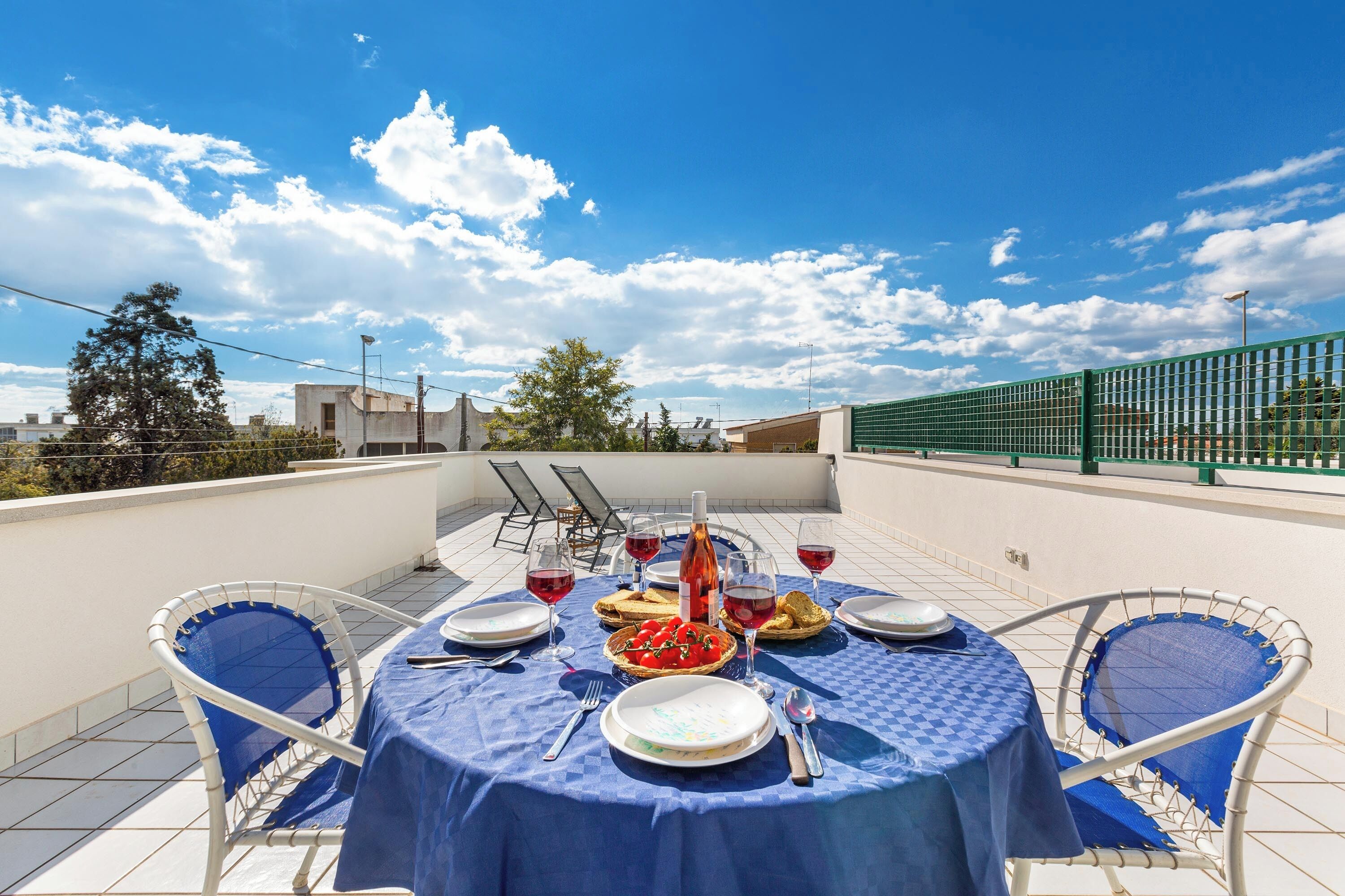 A rooftop terrace with a table set for a meal, including plates, glasses, and a bottle of wine.