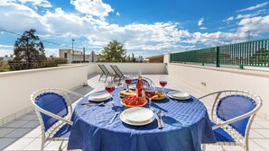 Eine Dachterrasse mit einem Esstisch, komplett mit Geschirr, Gläsern und einer Weinflasche.
