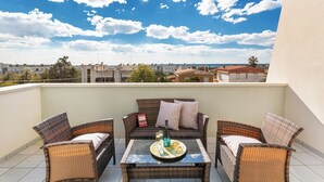 Un balcon agrémenté de meubles en osier, d’une table en verre et d’une bouteille de champagne.