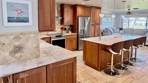 A modern kitchen with wooden cabinets, a stainless steel refrigerator, and a marble countertop.