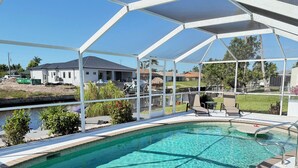 A clear swimming pool with a covered patio area, a view of a residential neighborhood, and a small water feature.