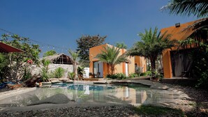 A pool area with a stone pathway, palm trees, and a building with orange walls.