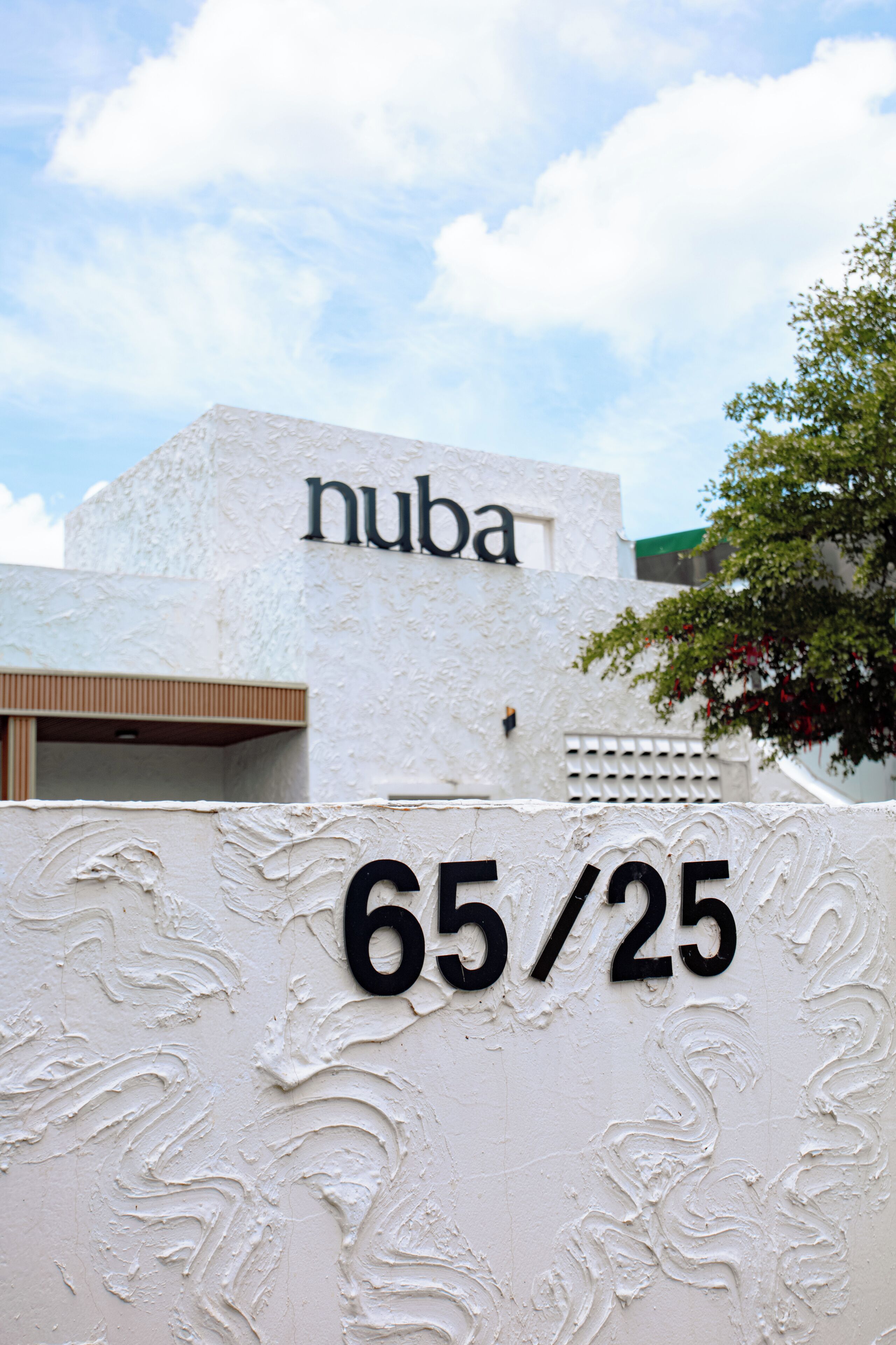 A building with a white facade and the name 'nuba' on it. There is a sign with '65/25' on a textured wall.