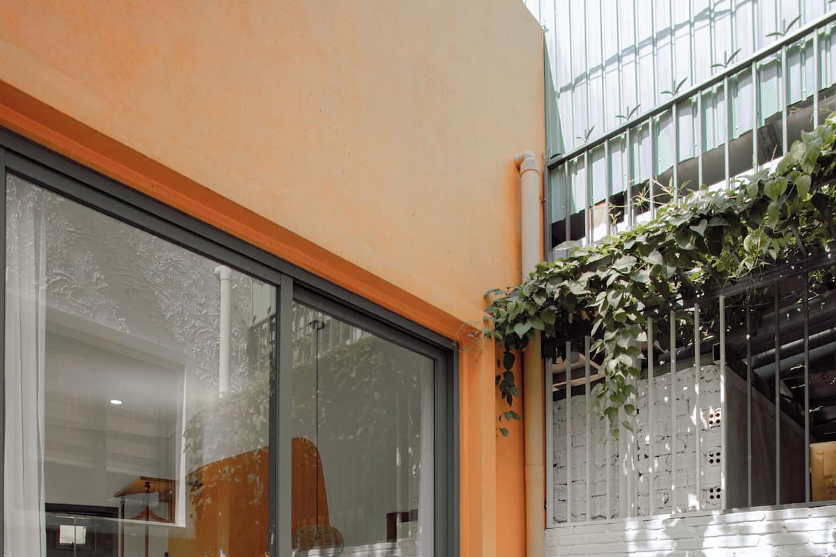 Une terrasse avec une table et des chaises, une porte vitrée donnant sur une pièce et un mur en briques blanches.